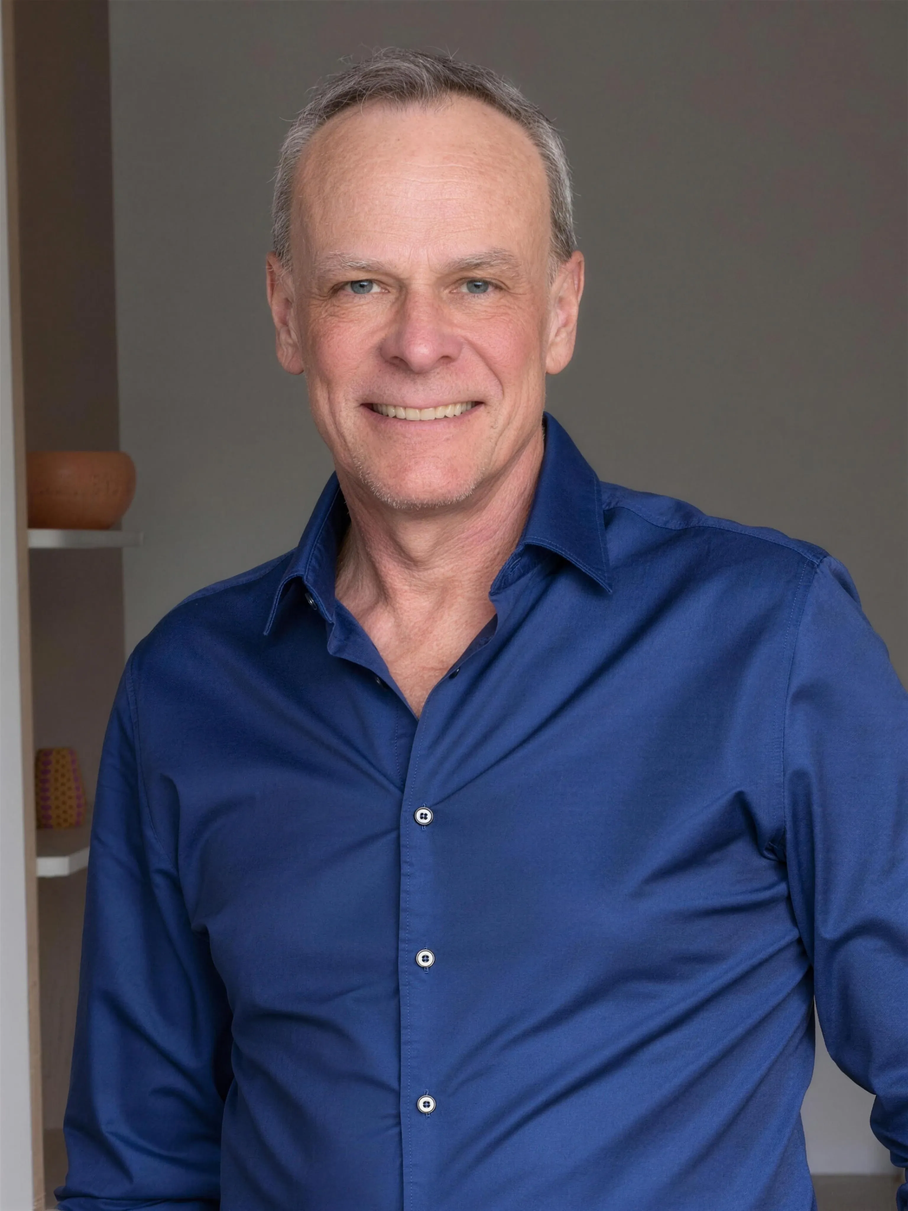 Pierre-André Gremaud, en chemise bleue, souriant face à l’objectif, devant un mur clair.